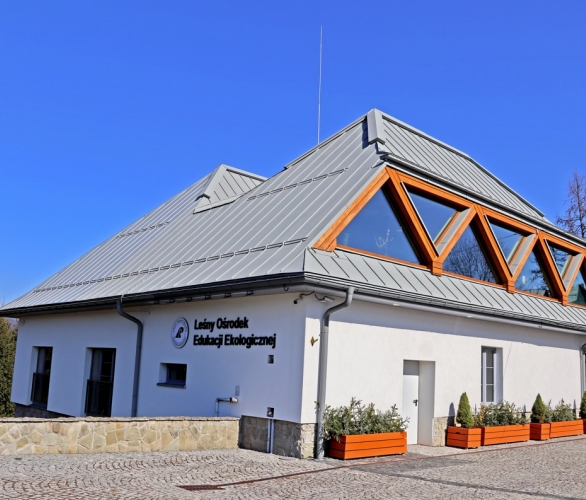 Budynek Leśnego Ośrodka Edukacyjnego w Istebnej.Biały,pokryty spadzistym dachem,w tle niebieskie niebo.